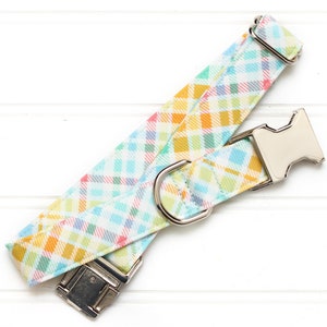 Puede incluir: Un collar de perro de cuadros de colores con una hebilla y un anillo en D plateados.