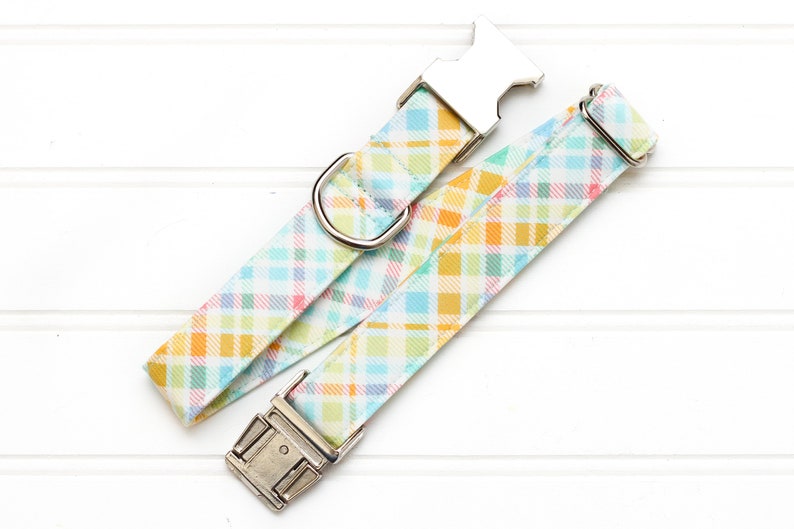 Puede incluir: Un collar de perro de cuadros azul claro y amarillo con herrajes plateados.