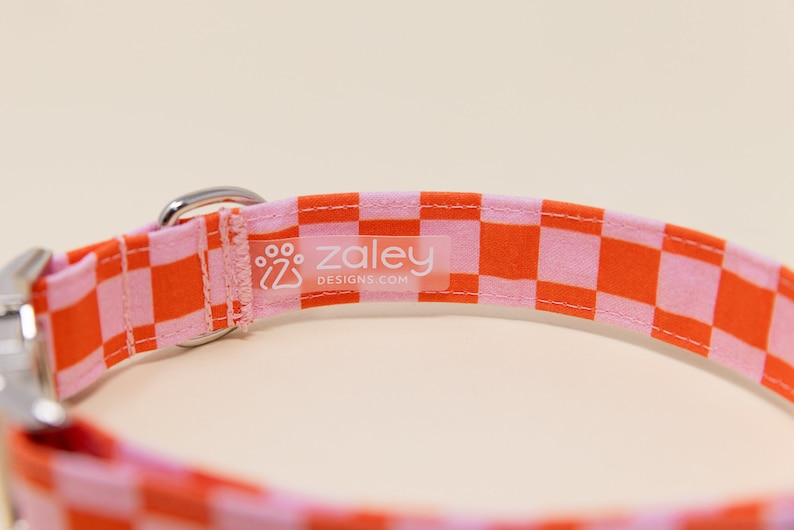 Op de afbeelding: Oranje en roze geruite hondenriem met een zilveren gesp en een wit label met de tekst "zaley designs.com"