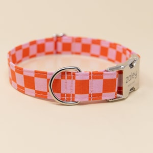 Op de afbeelding: Een roze en oranje geruite hondenriem met een zilveren gesp en een zilveren D-ring. De gesp heeft de tekst "Zoley Designs" gegraveerd.