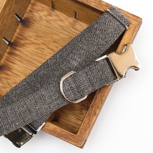 Puede incluir: Un collar de perro de color gris y negro con estampado de espiga, con hebilla y anilla en D plateadas.