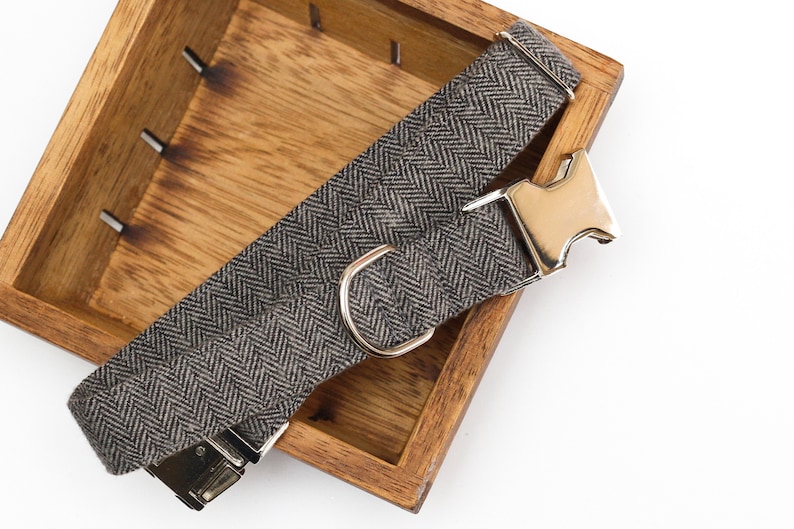 Puede incluir: Un collar de perro de color gris y negro con estampado de espiga, con hebilla y anilla en D plateadas.