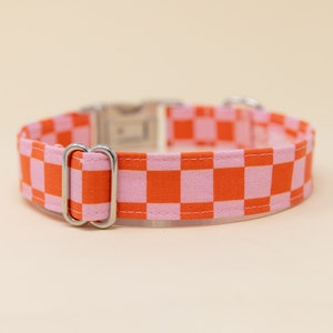 Op de afbeelding: Een roze en oranje geruite hondenriem met een zilveren gesp en D-ring.