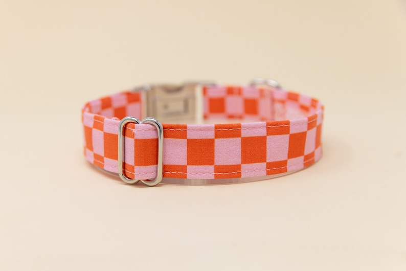 Op de afbeelding: Een roze en oranje geruite hondenriem met een zilveren gesp en D-ring.