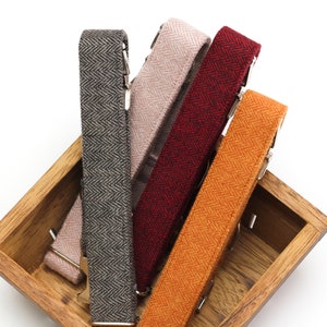 Puede incluir: Cuatro tirantes de tela en una caja de madera. Los tirantes son de diferentes colores y patrones: gris espiga, rosa espiga, rojo espiga y naranja espiga.