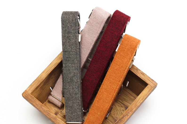 Puede incluir: Cuatro tirantes de tela en una caja de madera. Los tirantes son de diferentes colores y patrones: gris espiga, rosa espiga, rojo espiga y naranja espiga.