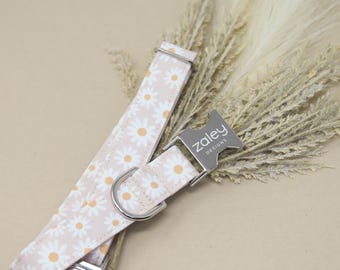 May include: A pink and white dog collar with a daisy print and a silver buckle that says "zaley designs".