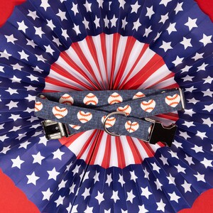 Puede incluir: Un collar de perro azul y blanco con un estampado de coraz&oacute;n rojo y b&eacute;isbol. El collar est&aacute; encima de un abanico de papel rojo, blanco y azul.