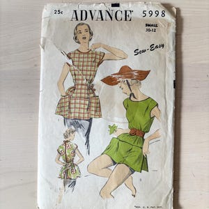 Peut inclure: Une pochette de patron de couture vintage Advance 5998 pour taille small 10-12. La couverture présente des illustrations de deux tenues : un haut à carreaux avec poches et une robe verte avec ceinture et chapeau marron, et une vue arrière.