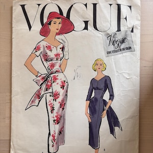 May include: A vintage Vogue Couturier Design sewing pattern. The pattern features illustrations of two dresses: a floral print dress with a bow and a solid-coloured dress with a draped back. The Vogue logo is prominently displayed.