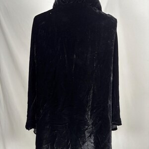 May include: A long, black velvet coat with a large, rounded collar. The coat is displayed on a mannequin, showcasing its flowing design and luxurious texture. The fabric appears to have a subtle sheen.