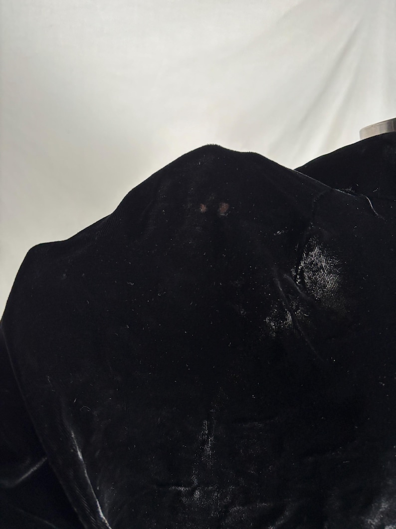 May include: Close-up of a black velvet fabric. The fabric has a soft, lustrous appearance with visible texture and slight variations in color. The image highlights the rich, dark color and the tactile quality of the material.