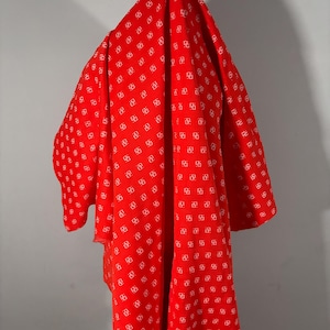 May include: A red fabric with a white geometric pattern is draped over a form. The fabric is a vibrant red with a repeating design of white squares, creating a visually appealing contrast. The fabric appears to be lightweight and flowing.