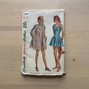 May include: A vintage Simplicity printed pattern envelope. The illustration shows two women in clothing. One is in a striped coat and shorts, the other in a polka dot dress. The envelope is marked "2441" and "Size 14 Bust 81cm".
