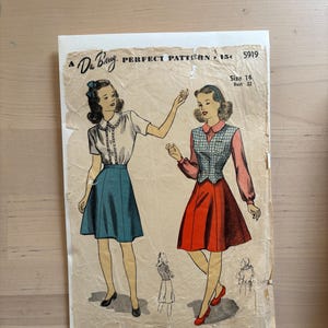 May include: Vintage sewing pattern featuring illustrations of two women in dresses. The pattern is labeled "Du Barry Perfect Pattern" with text indicating size 14 and bust 32. The paper has a worn, aged appearance.