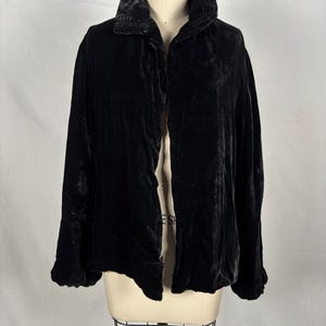 Könnte beinhalten: Schwarze Samtjacke mit breitem Kragen und langen Ärmeln. Die Jacke wird auf einer Schaufensterpuppe präsentiert. Der Stoff wirkt weich und hat einen leichten Glanz.