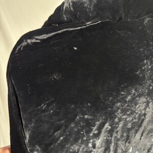 May include: Close-up of a black velvet jacket. The fabric has a soft, textured appearance with subtle variations in tone. The jacket features a pocket on the left side. The overall impression is one of luxury and elegance.