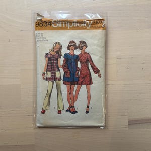 Puede incluir: Un patrón de costura Simplicity vintage, talla 9jp, con ilustraciones de tres mujeres con vestidos y atuendos de los años 70. El patrón incluye medidas de busto de 84 cm y cintura de 62 cm, y es para tallas Junior Petite. El patrón está en una funda de plástico transparente.