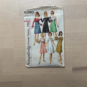 May include: A vintage Simplicity sewing pattern, size 85, with illustrations of dresses. The pattern cover shows the number 6260, and text indicating it's a sub-teen pattern. The cover is printed in Canada and is on a light wooden surface.
