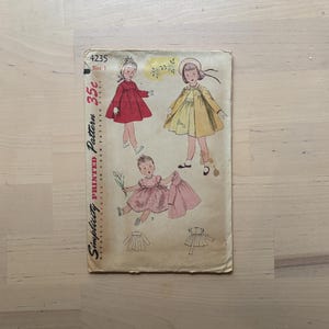 May include: Vintage Simplicity printed pattern 4235, size 1. The cover features illustrations of children's dresses in red, yellow, and pink. The pattern includes details printed on each pattern piece.