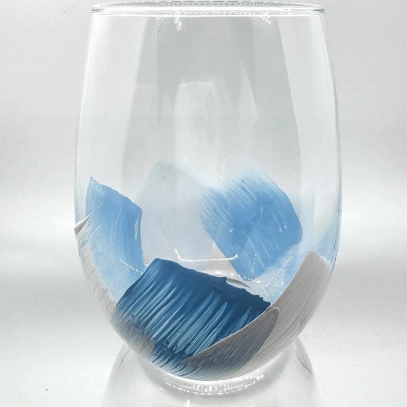 May include: A clear glass wine glass with blue and white abstract brushstrokes painted on the outside.