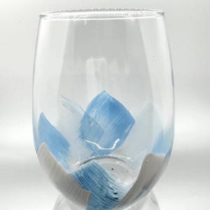 May include: A clear glass wine glass with a blue and white abstract design painted on the side.
