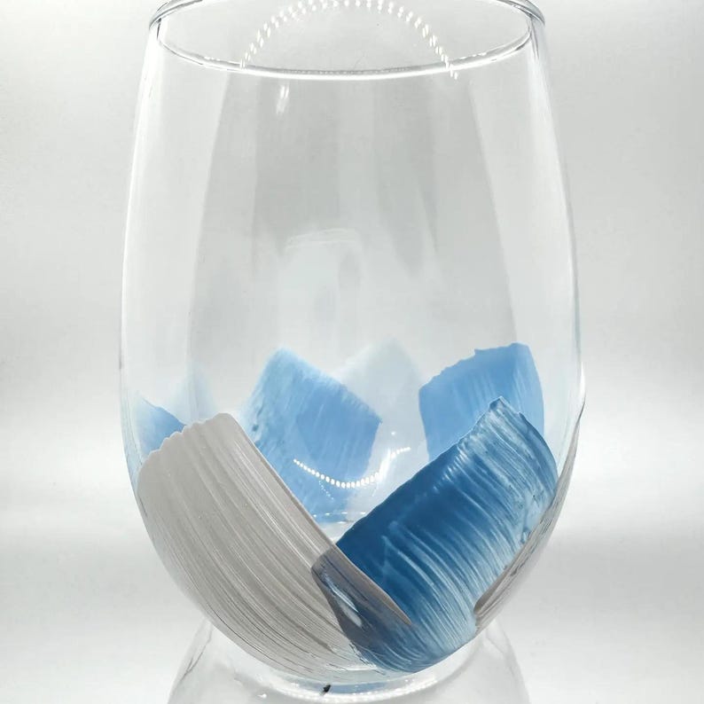 May include: A clear glass wine glass with blue and white brushstrokes painted on the inside.