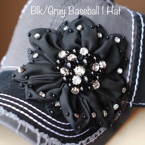 May include: Black and gray baseball hat with a decorative black flower. The flower is embellished with rhinestones and black beads. The hat has a distressed look with white stitching.