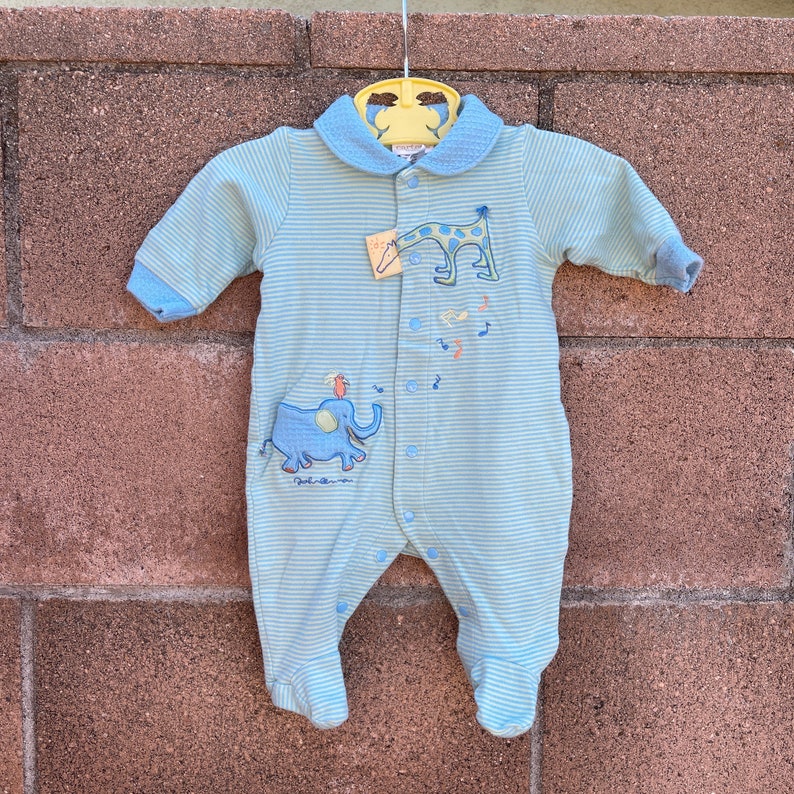 Puede incluir: Un pelele de beb&eacute; a rayas azules y blancas con una aplicaci&oacute;n de jirafa y elefante. El pelele tiene un cuello blanco y un cierre de botones.