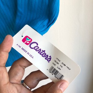 May include: A white tag with the Carter's logo and text that reads "STYLE 038-452 COLOR TO SIZE 12M K-740 MADE IN U.S.A."  A barcode is below the text.
