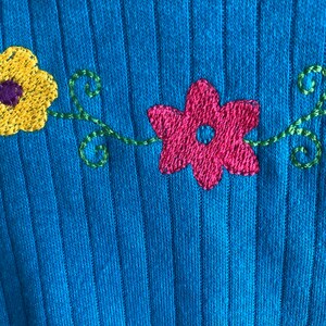 May include: A blue ribbed jumper with embroidered flowers in yellow, pink, and green.