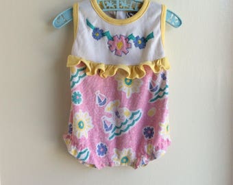 May include: A pink and white baby onesie with a yellow ruffle trim and a floral design. The onesie has a sleeveless design and a snap closure at the bottom.