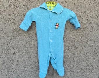 May include: A light blue baby onesie with a white trim and a Winnie the Pooh embroidered design.