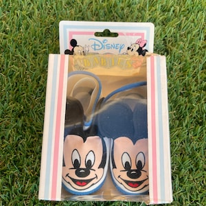 May include: A pair of blue and white baby shoes with Mickey Mouse faces on them. The shoes are in a box with a Disney Babies label.