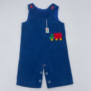 May include: Blue corduroy overalls with a red truck applique and a traffic light detail. The overalls have white snaps and are for a baby or toddler.