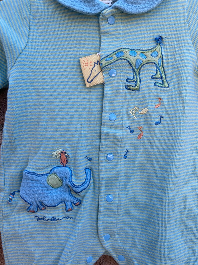 Puede incluir: Un pelele de beb&eacute; a rayas azules y verdes con un dise&ntilde;o bordado de elefante y jirafa. El pelele tiene un cuello azul y se abrocha con botones en la parte delantera.