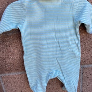 Puede incluir: Un pelele de beb&eacute; a rayas azules y blancas con cuello. El pelele est&aacute; hecho de una tela suave y c&oacute;moda y tiene un cierre de presi&oacute;n en la parte inferior.