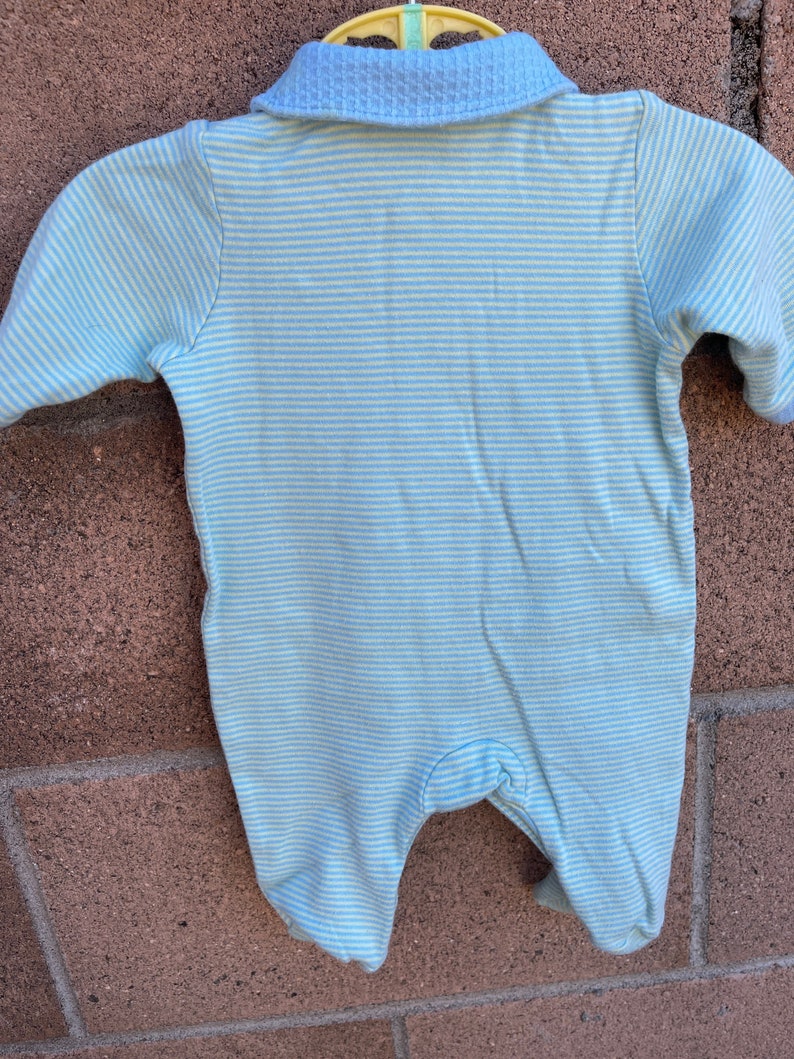 Puede incluir: Un pelele de beb&eacute; a rayas azules y blancas con cuello. El pelele est&aacute; hecho de una tela suave y c&oacute;moda y tiene un cierre de presi&oacute;n en la parte inferior.