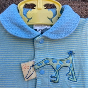 Puede incluir: Un mameluco de beb&eacute; a rayas azules y verdes con un cuello amarillo y una aplicaci&oacute;n de jirafa. El mameluco tiene cierre de botones y el texto "Carter's Baby" en la etiqueta.