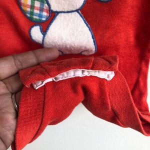 Puede incluir: Mono de beb&eacute; rojo con un cachorro blanco bordado con orejas a cuadros. El mono tiene un ribete blanco alrededor del cuello.