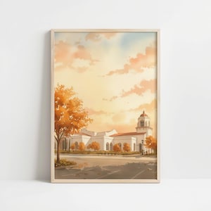 May include: Watercolor print of a building with a domed tower, set against a sunset sky. The building is white with a red-tiled roof. Trees with orange leaves frame the building. The artwork is in a wooden frame.