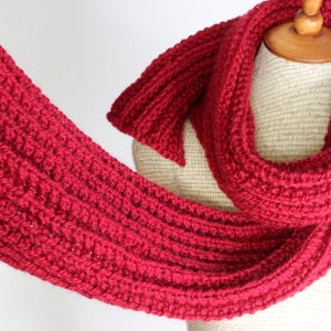 May include: A red knitted scarf with a textured pattern. The scarf is draped over a mannequin.