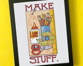 May include: Framed cross-stitch art with the words "MAKE STUFF." The artwork features craft supplies: glue, scissors, tape, paintbrushes, pencils, and a ruler. The color palette includes red, blue, green, yellow, and beige.