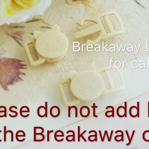 May include: Two beige plastic breakaway buckles for cat collars. The buckles have a cat face design and the text "Breakaway buckle for cat" is written on the image. The text "Please do not add leash to the Breakaway collar!" is written in red.