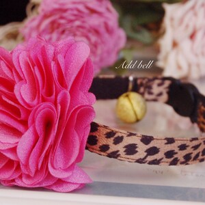 May include: A pink flower-shaped cat collar with a leopard print band and a small gold bell. "Add bell" is written on the collar.