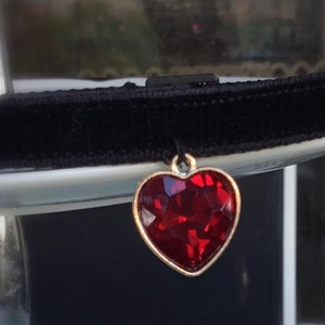 Puede incluir: Un collar gargantilla de terciopelo negro con un colgante en forma de corazón rojo.