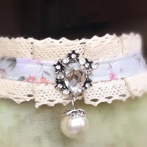 May include: A delicate white lace choker with a floral ribbon and a dangling pearl and crystal pendant.