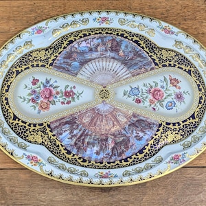 May include: Oval decorative serving tray with a light blue background and a gold rim. The tray features floral and fan designs, with a central image of a landscape scene. The tray is approximately 18 inches long.