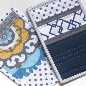May include: Two rectangular quilted fabric pot holders. One features a yellow, blue, and gray floral pattern with a white and gray polka dot border. The other displays a navy blue section, a white and blue geometric pattern, and a gray polka dot border.