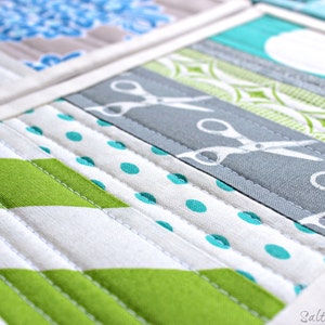 May include: A quilted fabric piece featuring horizontal strips of various patterns including lime green chevrons, white fabric with teal polka dots, and a grey strip with a white scissor print. The text Saltwater Quilts is visible in the bottom right corner.
